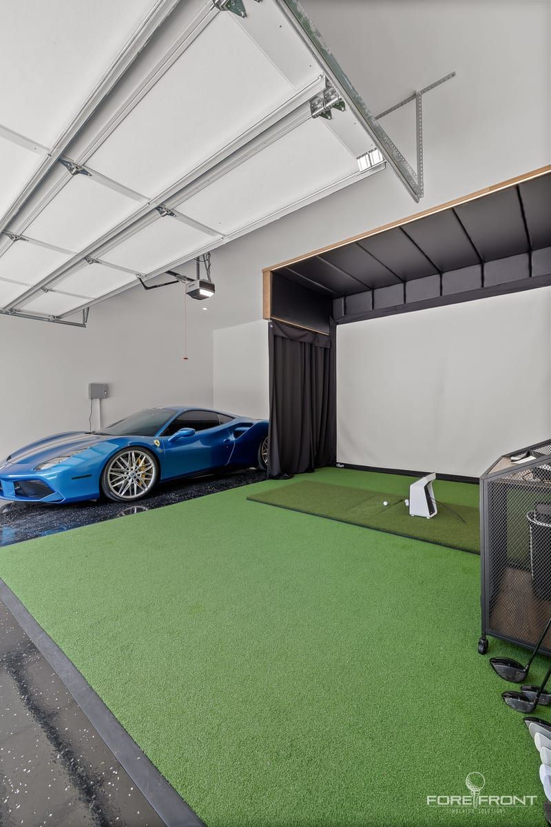 A garage converted to a golf simulator bay, turf laid over the floor beside a parked car.