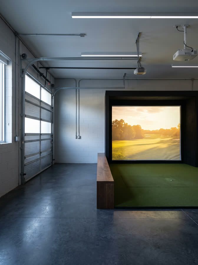 A garage converted to a golf simulator bay, the sectional door and painted blockwork still visible beside the finished screen recess.