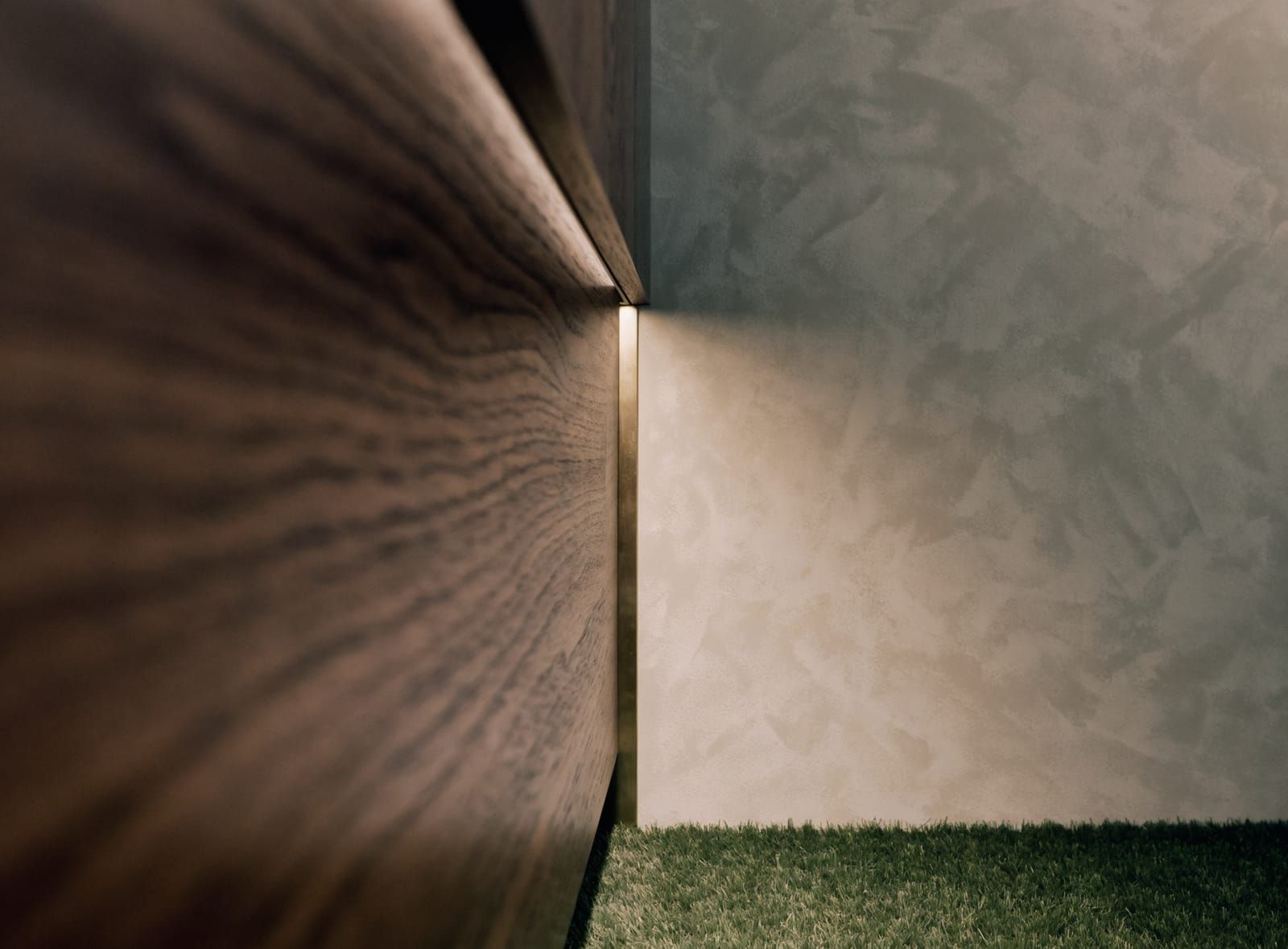 Finish detail: a walnut cabinet edge meeting plaster with a brass reveal, lit from above, turf underfoot