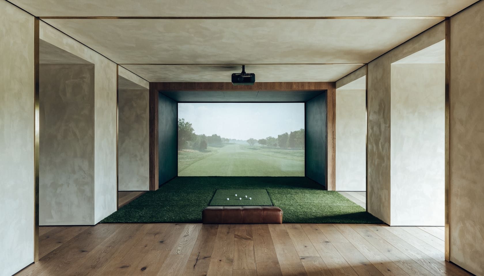 A purpose-built indoor golf bay: an impact screen filling a walnut-framed recess, a ceiling-mounted projector, and a hitting mat with balls on short turf